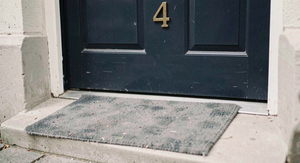 A dark blue front door with a brass numeral four, a smooth concrete ramp rising to the threshold and a worn grey doormat
